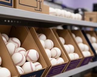 練習用ボールと試合球をチーム別に箱へ整理した野球用品店の棚